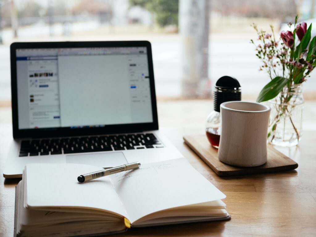 Skrivebok med penn, en laptop og en kaffekopp på et bord. Foto