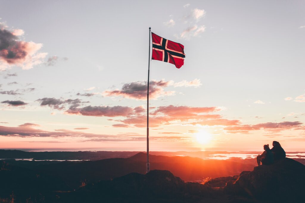 Norsk flagg på flaggstang i solnedgang.